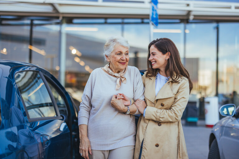 Elderly woman and younger woman clasp hands and smile while engaging in conversation outside under natural light. A representation of family love and intergenerational connection.